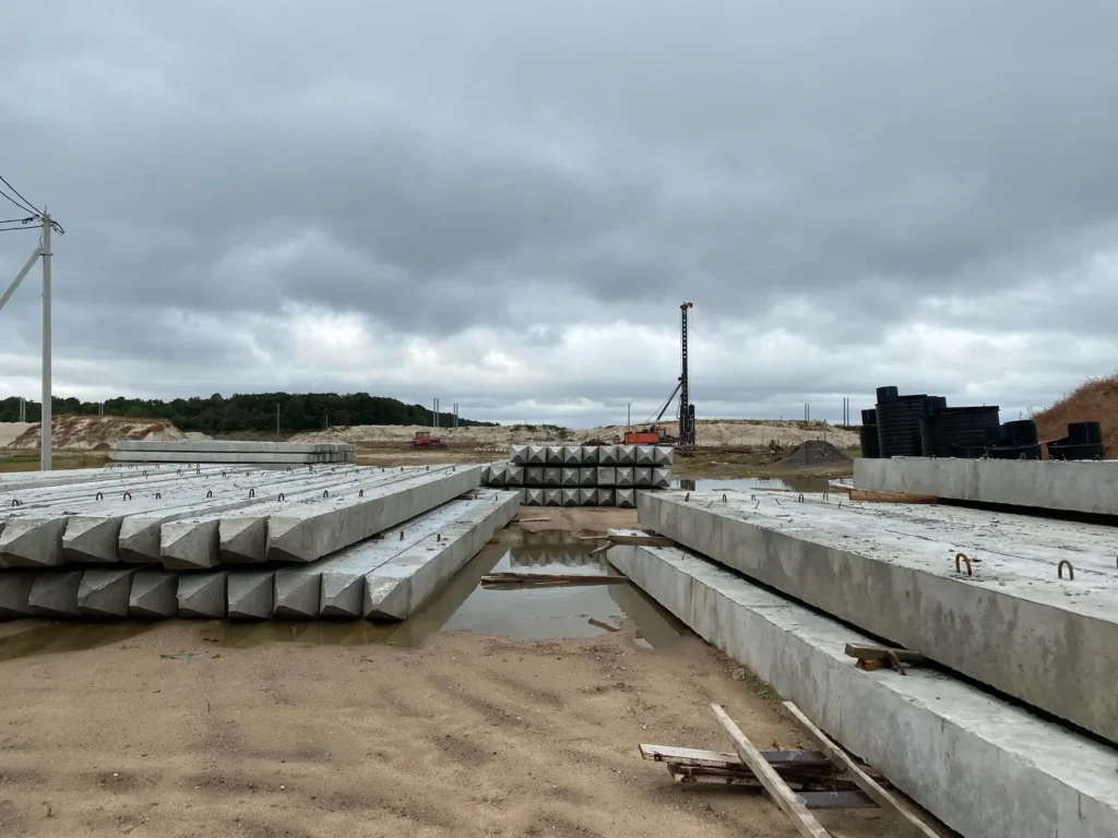 Betonowe fundamenty z widocznym zbrojeniem na tle części placu budowy.